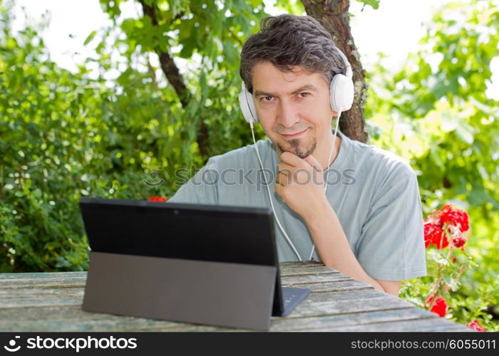 young man holding a tablet with headphones, outdoor