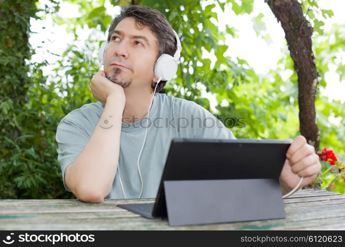 young man holding a tablet with headphones, outdoor