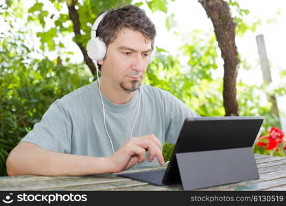 young man holding a tablet with headphones, outdoor