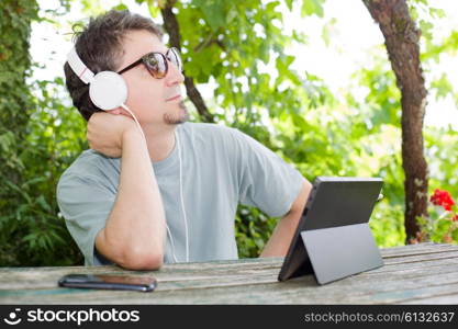 young man holding a tablet with headphones, outdoor