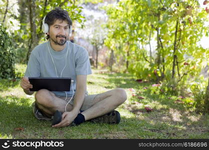 young man holding a tablet with headphones, outdoor