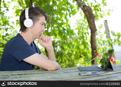 young man holding a tablet with headphones, outdoor