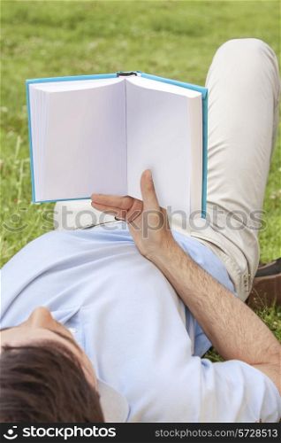 Young man holding book while lying in park