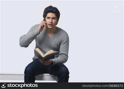 Young man holding book while talking on phone