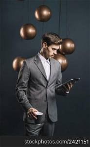 young man holding disposable coffee cup looking digital tablet standing front streamlined mirror round copper chandelier
