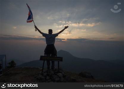 Young man holding flag to conquer the mountain. Silhouette style. subject is blurred and low key.