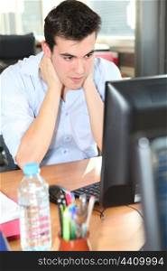 Young man holding his neck in front of a desktop computer