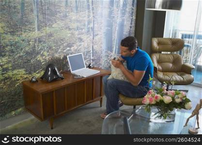 Young man holding his pet and sitting in front of a laptop