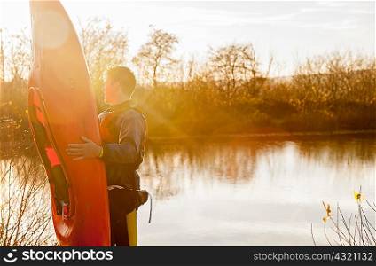 Young man holding kayak by lake