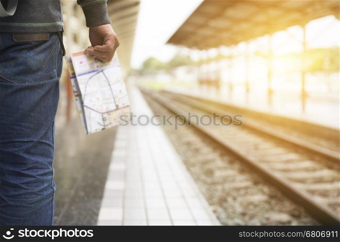 young man holding map standing on platform at train station - travel concept