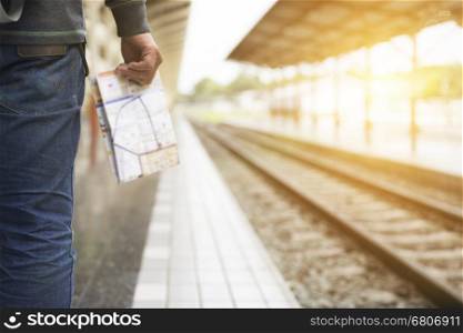 young man holding map standing on platform at train station - travel concept