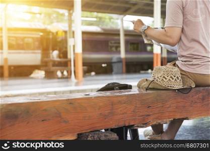 young man holding map with backpack sitting on platform at train station - travel concept