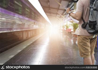 young man holding map with backpack standing on platform at train station - travel concept