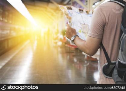 young man holding map with backpack standing on platform at train station - travel concept