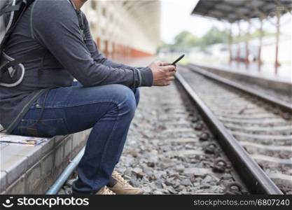 young man holding mobile phone standingon platform at train station - travel concept