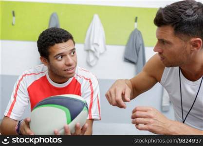 young man holding rugby ball talking to coach