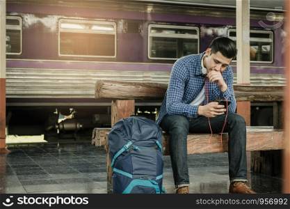 Young man holding smart phone and using music playlist with waiting train at station.