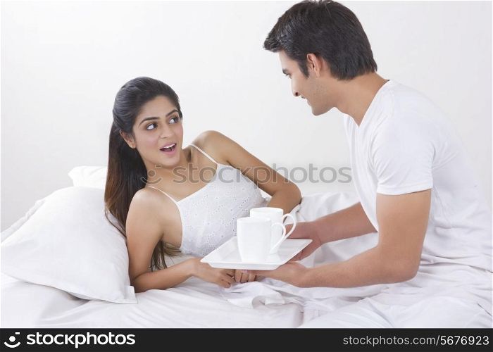 Young man holding tray of coffee cups by surprised woman in bed