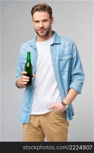 Young Man holding wearing jeans shirt Bottle of beer standing over Grey Background.. Young Man holding wearing jeans shirt Bottle of beer standing over Grey Background