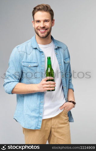 Young Man holding wearing jeans shirt Bottle of beer standing over Grey Background.. Young Man holding wearing jeans shirt Bottle of beer standing over Grey Background