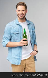 Young Man holding wearing jeans shirt Bottle of beer standing over Grey Background.. Young Man holding wearing jeans shirt Bottle of beer standing over Grey Background