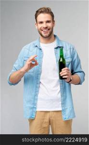 Young Man holding wearing jeans shirt holding Bottle of beer standing over Grey Background.. Young Man holding wearing jeans shirt holding Bottle of beer standing over Grey Background