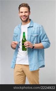 Young Man holding wearing jeans shirt holding Bottle of beer standing over Grey Background.. Young Man holding wearing jeans shirt holding Bottle of beer standing over Grey Background