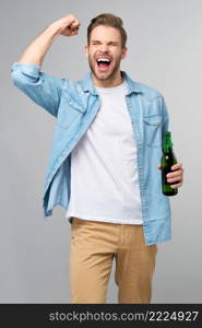 Young Man holding wearing jeans shirt holding Bottle of beer standing over Grey Background.. Young Man holding wearing jeans shirt holding Bottle of beer standing over Grey Background