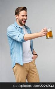 Young Man holding wearing jeans shirt holding glass of beer standing over Grey Background.. Young Man holding wearing jeans shirt holding glass of beer standing over Grey Background