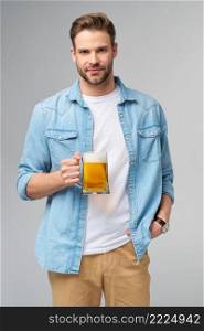 Young Man holding wearing jeans shirt holding glass of beer standing over Grey Background.. Young Man holding wearing jeans shirt holding glass of beer standing over Grey Background