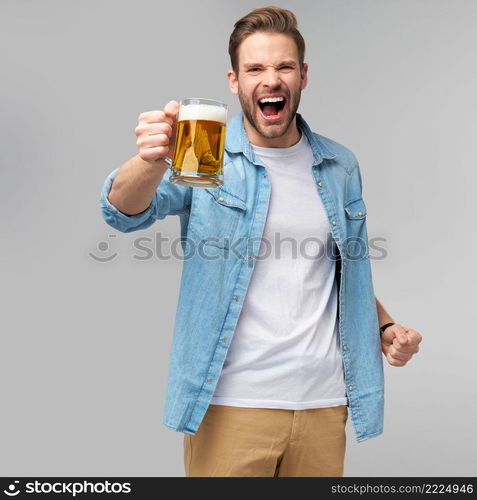 Young Man holding wearing jeans shirt holding glass of beer standing over Grey Background.. Young Man holding wearing jeans shirt holding glass of beer standing over Grey Background