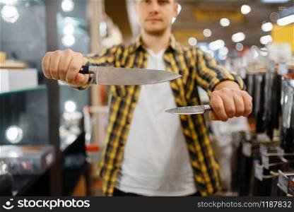 Young man holds kitchen knives in houseware store. Male person buying home goods in market, guy in kitchenware supply shop. Young man holds kitchen knives in houseware store