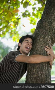 Young man hugging a tree trunk and laughing