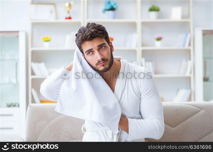 Young man in a bathrobe after shower drying hair with a towel