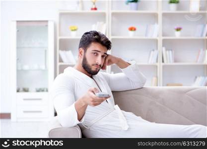 Young man in a bathrobe watching television at home on a sofa co. Young man in a bathrobe watching television at home on a sofa couch