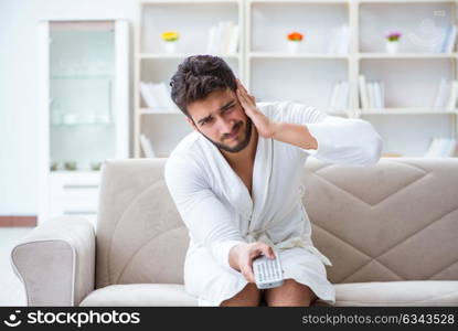 Young man in a bathrobe watching television at home on a sofa co. Young man in a bathrobe watching television at home on a sofa couch