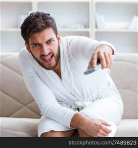 Young man in a bathrobe watching television at home on a sofa couch. Young man in a bathrobe watching television at home on a sofa co