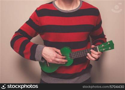 Young man in a striped jumper is playing ukulele