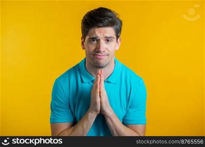 Young man in blue t-shirt praying over yellow background. Guy begging someone satisfy his desires, help with. Young man in blue t-shirt praying over yellow background. Guy begging someone satisfy his desires, help with.
