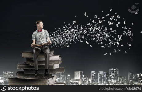 Young man in bow tie sitting with book in hands. Light of education