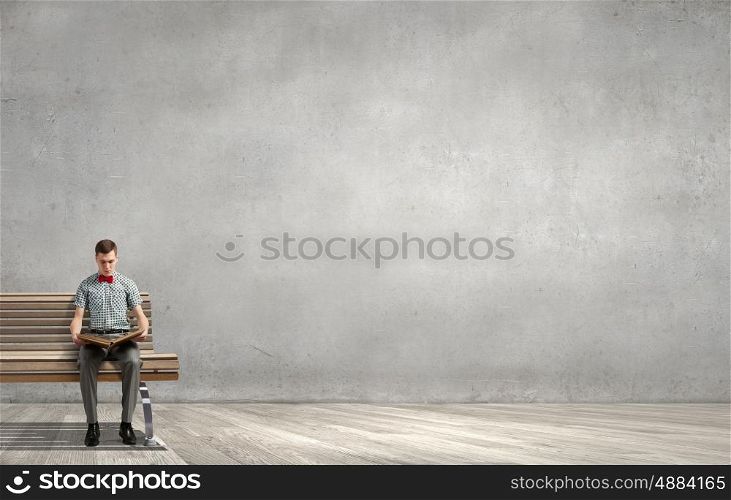 Young man in bow tie sitting with book in hands. Light of education