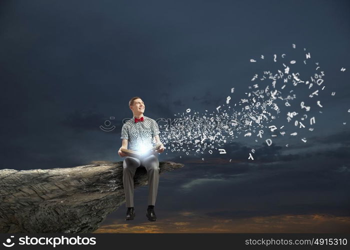 Young man in bow tie sitting with book in hands. Light of education