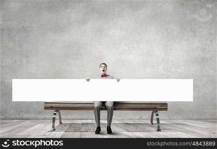 Young man in bow tie sitting with white blank banner . Place for your text