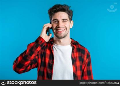 Young man in bright colorful wear talking on mobile cell phone on blue background. Trendy guy have conversation. Smartphone, technology concept. Young man in bright colorful wear talking on mobile cell phone blue background