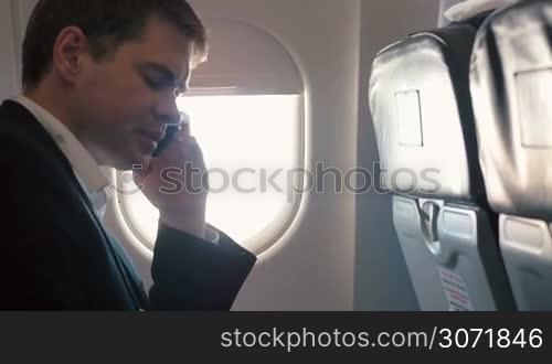 Young man in business trip. He traveling by plane and talking on the phone sitting by the illuminator