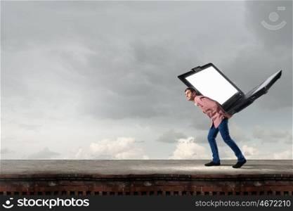 Young man in casual carrying big laptop on back. Guy carrying laptop
