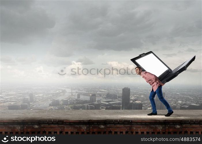 Young man in casual carrying big laptop on back. Guy carrying laptop