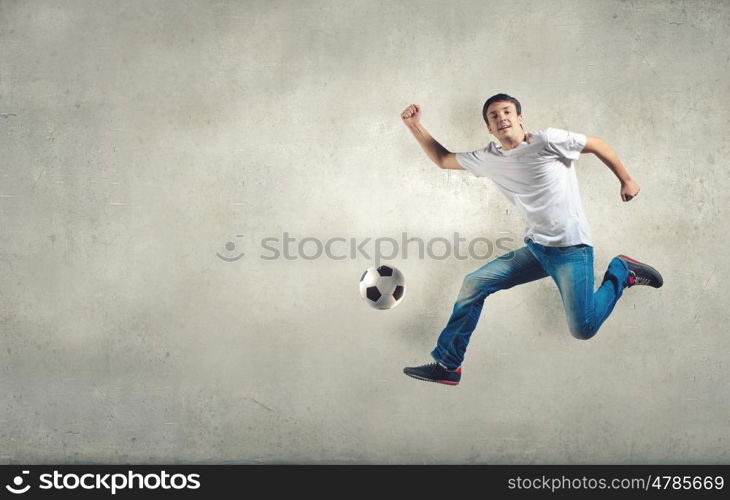 Young man in casual jumping to hit the ball. Football fan