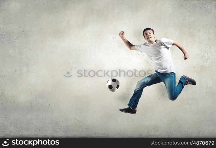 Young man in casual jumping to hit the ball. Football fan