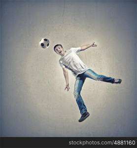 Young man in casual jumping to hit the ball. Football fan